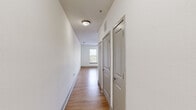 This single-floor residence presents a clean, modern aesthetic throughout its well-organized layout. The kitchen serves as a functional centerpiece, featuring white shaker-style cabinetry, granite countertops, and a full suite of stainless steel appliances including a refrigerator, range, and built-in microwave. A peninsula with pendant lighting overhead defines the kitchen space, while large-format tile flooring grounds the area. A subway tile backsplash adds a classic touch.

The living and bedroom areas are finished with warm hardwood-style flooring and crisp white walls, creating a bright and inviting atmosphere. Multiple windows fitted with horizontal blinds allow generous natural light to fill the rooms and offer views of the surrounding neighborhood. A ceiling fan in the bedroom provides additional comfort and airflow.

A hallway connects the main living spaces to additional rooms, lined with panel-style doors in a neutral gray finish and illuminated by a flush-mount ceiling fixture. The bathroom is outfitted with light tile flooring, a soaking tub with subway tile surround, and clean white fixtures throughout. The overall design is cohesive, minimal, and move-in ready.