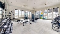 Located in Commerce City, Colorado, this fitness center offers a well-appointed and generously proportioned workout space across a single floor. The gym's design emphasizes openness and natural light, with large windows lining multiple walls and providing views of the surrounding neighborhood. The bright, neutral-toned interior is complemented by light herringbone-patterned carpet flooring and high ceilings fitted with ceiling fans for comfortable air circulation throughout the space.

The facility is comprehensively equipped to support a wide range of fitness routines. A dedicated cardio zone features multiple treadmills, elliptical trainers, and a stair climber, all positioned along the windowed walls to take advantage of the natural light and outdoor views. The strength training area includes a variety of cable and selectorized resistance machines, adjustable weight benches, and a full rack of dumbbells for free weight exercises. A functional training corner rounds out the offerings with stability balls and additional accessories for flexibility and balance work.

The layout is thoughtfully organized to allow ample floor space between equipment zones, supporting safe and comfortable movement throughout the gym. The clean, modern aesthetic and abundance of natural light create an inviting and motivating environment suited to a broad range of fitness goals.