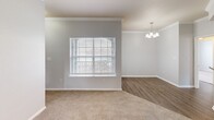 Located in San Marcos, TX, this single-floor, 3-bedroom, 3-bathroom home offers a well-designed layout with a blend of comfort and functionality. The combined kitchen and living area serves as the heart of the home, where the kitchen features white cabinetry, dark granite-style countertops, a breakfast bar peninsula, and black appliances, including a range and refrigerator. Hardwood-style flooring runs through the kitchen and dining area, while plush carpet extends throughout the living and bedroom spaces. The living room is accented with crown molding, a ceiling fan, and a window that brings in natural light, and flows seamlessly into a dining nook illuminated by an elegant chandelier. The primary bedroom is generously sized, offering a ceiling fan, a large window, and two doors — one leading to the en-suite bathroom and another to a spacious walk-in closet outfitted with wire shelving on multiple walls. The primary bathroom includes a double-sink vanity with dark countertops, white cabinetry, and a large mirror with vanity lighting. The additional bedrooms feature soft carpet and bright, neutral walls. Bathrooms are fitted with clean white tiled tub-shower combos and chrome fixtures throughout. Crown molding and consistent neutral tones give the entire home a cohesive, polished feel.