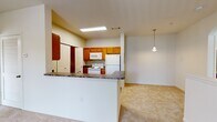 This residential unit is thoughtfully designed across multiple levels, connected by a carpeted staircase illuminated by an overhead light fixture. The open-concept kitchen serves as a functional centerpiece, featuring warm honey-toned wood cabinetry, dark granite-style countertops, and white appliances including a range, microwave, and refrigerator. A peninsula counter separates the kitchen from the adjoining living area, which is finished with plush neutral carpeting. A pendant light adds a finishing touch to the dining and living space. The kitchen also includes a convenient pantry closet with louvered bifold doors and rich dark hardwood-style flooring.

The bathrooms are finished consistently with dark hardwood-style flooring, warm wood vanity cabinetry, light countertops, and tiled shower-tub combinations. A well-lit vanity mirror provides ample lighting in each bathroom.

The bedrooms are generously sized, carpeted, and bathed in natural light through large windows with outdoor greenery views. Ceiling fans are featured in multiple rooms for added comfort. The primary living area opens directly to a private balcony through sliding glass doors with vertical blinds, offering pleasant outdoor views. Throughout the unit, neutral tones and clean finishes create a cohesive, comfortable atmosphere.