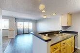 Located at 717 Seventh St in downtown Des Moines, Iowa, this one-bedroom, one-bathroom unit offers a well-organized floor plan designed for functional, comfortable living. A welcoming entrance hallway with hardwood-style flooring leads into the combined kitchen and living area, which serves as the heart of the unit. The living room is bright and open, benefiting from large sliding glass doors that flood the space with natural light and offer views of the surrounding cityscape. The kitchen is thoughtfully laid out with warm wood cabinetry, dark countertops, a double-basin sink, and full appliances including a refrigerator and dishwasher. A peninsula counter provides a natural division between the kitchen and living space while maintaining an open feel. The bedroom is a comfortable, carpeted retreat featuring a window with urban views and access to ample closet storage — with two closets serving the unit overall. The bathroom is well-appointed with light wood cabinetry, a dark stone-topped vanity with an undermount sink, a full tub and shower combination, and tile flooring. Textured ceilings and neutral-toned walls throughout lend the unit a clean, understated aesthetic well-suited to a variety of personal styles.