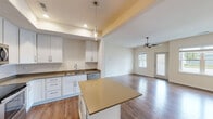 This single-floor residence offers a thoughtfully designed open-concept layout that seamlessly connects the kitchen and living area. The kitchen is a standout feature, equipped with white shaker-style cabinetry, stainless steel appliances including a refrigerator, range, microwave, and dishwasher, complemented by neutral-toned countertops. A central island provides additional prep space and casual seating, while a stylish pendant light adds a decorative touch. Recessed lighting and a tray ceiling further define the kitchen zone. Rich hardwood-style flooring flows throughout the main living areas, enhancing the warm, cohesive aesthetic. The spacious living room benefits from natural light through large windows and a glass-panel exterior door, and is finished with a ceiling fan overhead. Bedrooms feature soft carpeting, ceiling fans, and ample closet space, with one room offering a generous sliding-door closet and outdoor-facing window. The full bathroom includes a tub-shower combination, white vanity cabinetry with a dark countertop, and hardwood-style flooring. An attached garage with an automatic opener rounds out the practical amenities of this well-finished, move-in ready home.