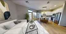 Located at 4739 N Scottsdale Rd in Scottsdale, AZ, this 720-square-foot, one-bedroom, two-bathroom apartment offers a well-designed single-floor layout. The open-concept living, dining, and kitchen area is anchored by a large island with a light countertop, warm wood cabinetry, and bar seating. The kitchen is equipped with stainless steel appliances including a gas range, microwave, and refrigerator, complemented by white shaker cabinets and a tile backsplash. Pendant lighting and recessed ceiling lights illuminate the space, while wood-look flooring runs throughout the main living areas. The living room features tall windows and a glass door that invite natural light and outdoor views. The primary bedroom spans 150 square feet with warm-toned walls and hardwood-style flooring. The en-suite primary bathroom includes a double-sink vanity with white cabinetry, dark tile flooring, and a glass-enclosed walk-in shower with marble-style tile. A walk-in closet with built-in shelving and hanging rods connects to the bathroom. A second bathroom features a single vanity with a framed mirror. The dedicated laundry room houses a Whirlpool front-load washer and dryer with an adjacent water heater and closet space.