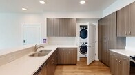 This thoughtfully laid-out single-floor residence offers three bedrooms, two bathrooms, and a practical, modern design throughout. The open living area greets you with warm light wood-style flooring, neutral walls, and a wall-mounted HVAC unit, with a door leading directly to a private balcony that overlooks a lush, landscaped green space and tree canopy — a standout feature of the home.

The kitchen is a functional centerpiece, outfitted with rich wood-toned cabinetry, white quartz countertops, stainless steel appliances including a range, microwave, and refrigerator, and recessed lighting overhead. A convenient in-unit stacked washer and dryer is tucked just off the kitchen, adding everyday practicality.

The bedrooms feature plush carpeting and closet space, including a walk-in closet with wire shelving and a sliding-door reach-in closet, providing ample storage. The bathrooms are clean and bright, with a full tub-shower combination, chrome fixtures, and a wall-mounted heater.

A hallway connects the rooms efficiently, and the overall palette of soft neutrals and natural wood tones gives the space a cohesive, contemporary feel throughout.