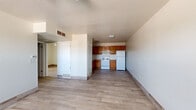 This 2-bedroom, 1-bathroom single-story unit offers a practical and efficiently designed layout with wood-look tile flooring running throughout the entire space. The open-concept living area flows directly into the kitchen, creating a cohesive shared space that maximizes usability. The kitchen is equipped with warm-toned oak cabinetry, a double-basin stainless steel sink, laminate countertops in an L-shaped configuration, a white electric range, and a full-size refrigerator — providing ample storage and prep space. A textured ceiling adds architectural character to the kitchen and living areas.

The living room receives natural light through a window with blinds and features a ceiling fan with light fixture, along with a front entry door. Both bedrooms continue the wood-look tile flooring and are finished with neutral walls and natural light from windows with blinds. The primary bedroom includes a sliding-door closet with built-in shelving and hanging rod. The bathroom is appointed with a wood-vanity cabinet, an integrated sink with countertop, and a full walk-in shower enclosure clad in large-format dark tile. The unit offers a clean, functional aesthetic throughout.