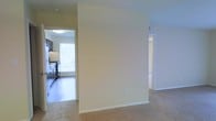 This single-floor residence offers a straightforward and functional layout designed for comfortable everyday living. The interior is characterized by neutral, warm-toned walls that create a bright and welcoming atmosphere throughout the space.

The living area features soft wall-to-wall carpeting, providing a cozy and comfortable feel underfoot. A partial dividing wall separates the living space from the kitchen, offering a sense of definition between the two areas while maintaining an open and connected flow.

The kitchen is outfitted with stainless steel appliances, including a range, and features hard flooring that contrasts with the carpeted areas of the home. A window in the kitchen allows natural light to fill the space, enhancing the overall brightness of the interior.

Hallways lead to additional rooms, suggesting a thoughtful layout that keeps living and private spaces distinct. The clean white trim and baseboards throughout the unit add a crisp, polished finish to each room.

Overall, the space presents a practical and livable environment with a neutral palette, natural light, and a seamless connection between its key areas, making it a versatile and move-in ready home.