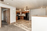 This two-floor residence offers a practical and well-appointed layout with consistent, warm finishes throughout. The main level features an open-concept design where the kitchen flows seamlessly into the dining and living areas. The kitchen is equipped with rich medium-toned wood cabinetry, granite-look countertops, and a full suite of black appliances including a refrigerator, electric range, over-the-range microwave, and dishwasher. A double basin sink is positioned beneath upper cabinets, maximizing storage and functionality. Light wood-look plank flooring runs through the kitchen and main living areas, adding warmth and visual continuity. An elegant chandelier serves as a focal point over the dining area, while a half-wall with wood cap detail neatly separates the kitchen zone from the living space. The living area transitions to plush carpet and is brightened by natural light from a window and accented by a ceiling fan. The staircase connects both floors, with the upper level hosting additional bedrooms, each carpeted and equipped with ceiling fans and windows that allow natural light. One bedroom features dual closet doors for added storage convenience. The bathroom includes a full tub-shower combo, a vanity with granite-look counters, dark wood cabinetry, and wood-look tile flooring, rounding out this functional and comfortable home.