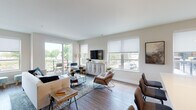This thoughtfully designed single-floor residence offers a contemporary layout that balances functionality with modern aesthetics. The open-concept living area serves as the centerpiece of the unit, featuring warm wood-look flooring, neutral wall tones, and an abundance of natural light streaming through multiple large windows fitted with roller shades. A sliding glass door connects the living space directly to a private balcony, offering pleasant outdoor views of surrounding greenery.

The kitchen is well-appointed with stainless steel appliances, including an electric range, built-in microwave, and refrigerator. Flat-front cabinetry in a warm wood tone is complemented by crisp white upper cabinets and light-colored countertops, creating a clean, contemporary workspace. A galley-style configuration maximizes efficiency along the layout.

The unit includes two bedrooms, each carpeted or finished with wood-look flooring and equipped with windows offering outdoor views. The primary bathroom is generously proportioned, featuring a long vanity with modern cabinetry, a glass-enclosed shower, and light wood-tone flooring. Throughout the unit, clean white doors, recessed lighting, and a cohesive neutral palette contribute to a polished, move-in-ready ambiance.