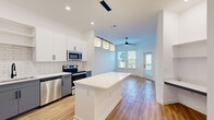 This single-floor residence in Clermont, FL offers a contemporary open-concept layout connecting the kitchen, dining, and living areas. The kitchen is well-appointed with stainless steel appliances, including a side-by-side refrigerator with ice maker, electric range, microwave, and dishwasher. Two-tone cabinetry pairs white upper cabinets with gray lower cabinets, complemented by a white subway tile backsplash, white quartz countertops, a black matte faucet, and a central island with pendant lighting overhead. A built-in desk nook adds a functional workspace adjacent to the kitchen. Wood-look flooring runs consistently throughout the unit, enhancing the cohesive design. The living area benefits from generous natural light through multiple windows and a glass door leading to an outdoor balcony, with a ceiling fan providing additional comfort. Bedrooms are spacious with tall ceilings, ceiling fans, and ample natural light. The bathroom features a gray vanity with white countertop, matte black hardware, a large mirror, and a glass-enclosed walk-in shower with tile surround. The overall aesthetic is clean, modern, and bright.
