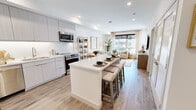 This single-floor residence offers a thoughtfully designed open-concept layout that seamlessly connects the kitchen, dining, and living areas into one bright, cohesive space. The contemporary kitchen is a standout feature, showcasing flat-panel light wood cabinetry extending to the ceiling, a full suite of stainless steel appliances including a refrigerator, range, dishwasher, and over-the-range microwave, and a sleek white quartz island with bar seating — ideal for both casual dining and entertaining. Light wood-tone flooring flows throughout the space, reinforcing a clean and modern aesthetic.

The living room is bathed in natural light from large windows that frame exterior views, complemented by recessed lighting and sheer drapery that add warmth and softness. The space is well-proportioned and inviting, with room for generous seating arrangements.

Two bedrooms provide comfortable retreats, each featuring large windows with roller shades, ceiling fans, and access to closet storage. The neutral palette and soft tones create a calm, restful atmosphere in each room.

The bathroom maintains the same modern sensibility with light tile flooring, a floating wood vanity, a white countertop, and clean white walls accented by tasteful décor. Overall, the residence presents a bright, airy, and well-appointed living environment with consistent contemporary finishes throughout.