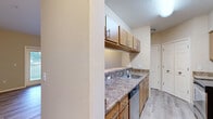 This single-floor unit offers a practical and comfortable layout designed for everyday living. The kitchen is a functional galley-style space outfitted with stainless steel appliances — including a range, over-the-range microwave, and refrigerator — complemented by warm medium-toned wood cabinetry, granite-style countertops, a stainless steel sink, and a built-in dishwasher. Light hardwood-style flooring runs throughout the kitchen and extends into the living areas, lending a clean and cohesive aesthetic. A double-door closet and additional storage are conveniently accessible from the kitchen area. The open living room is bright and welcoming, featuring light-toned walls, large windows with blinds that invite natural light, and direct access to an outdoor balcony. A fireplace mantel adds a charming architectural detail to the living space. The bedrooms are carpeted for comfort, with corner window placements that provide pleasant outdoor views and ample natural light. The bathroom features a granite-style vanity countertop, wood cabinetry, a large mirror, and a shower-tub combination. Throughout the unit, neutral warm tones, clean white trim, and six-panel doors create a cohesive and inviting atmosphere.