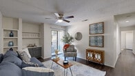 This single-floor residence offers a thoughtfully designed layout that balances comfort and functionality across multiple distinct living spaces. The living room serves as the heart of the home, featuring dark hardwood-style flooring, a textured ceiling with a ceiling fan, and a sliding glass door that fills the space with natural light while providing access to an outdoor area. Built-in shelving and a wet bar-style cabinet add both character and practicality to the room.

The kitchen is outfitted with gray shaker-style cabinetry, white quartz countertops, a subway tile backsplash, and black appliances including a dishwasher. A pantry closet provides additional storage, and the dark flooring continues seamlessly throughout.

Adjacent to the kitchen, the dining area offers an intimate setting highlighted by a drum pendant light and a built-in niche with mirrored backing — an elegant architectural detail ideal for display or storage.

The two bedrooms are comfortably sized, each featuring ceiling fans, textured ceilings, and large windows that invite natural light. The dark hardwood-style flooring carries through both rooms, contributing to a cohesive aesthetic.

The bathroom is clean and functional, with gray vanity cabinetry, a white quartz countertop, a full-size tub and shower combination, and wood-look flooring that ties the space together.