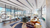 Located in the heart of Midtown Atlanta at 1301 Spring St NW, this striking amenity floor delivers a bold, eclectic design aesthetic that seamlessly blends comfort with contemporary style. The centerpiece of the space is a stylish wet bar clad in teal vertical tile, complete with bar seating, a mounted TV, and vibrant neon signage—ideal for social gatherings. Adjacent lounge areas feature oversized wingback chairs in rich jewel-toned upholstery, velvet sofas, and artfully layered rugs, creating inviting conversation zones throughout.

Floor-to-ceiling glass walls flood the interior with natural light and offer expansive views of the surrounding Midtown skyline, while providing a seamless visual connection to the outdoor terrace. The terrace itself is well-appointed with hanging egg chairs, a ping pong table, string lighting, a fireplace, and artificial turf seating areas—perfect for outdoor recreation and relaxation.

A dedicated private meeting room features a round dining-style table, sculptural wood chairs, a mounted display, rich burgundy wall covering, and warm accent lighting. A separate entertainment lounge includes a wall-mounted TV, linear fireplace, decorative shelving with curated objects, and large-format art. Bold, patterned area rugs and eclectic furnishings tie the entire floor together with artistic cohesion.