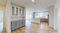 This well-appointed 3-bedroom, 2-bathroom single-floor residence offers a thoughtfully designed open-concept layout with modern finishes throughout. Light wood flooring flows seamlessly across the main living areas, complementing the bright, neutral color palette that creates an airy and inviting atmosphere.

The kitchen is a standout feature, showcasing a large central island with a clean quartz-style countertop, two-tone cabinetry with white upper glass-front cabinets and slate-gray lower cabinets, subway tile backsplash, stainless steel appliances, and pendant lighting. A built-in buffet cabinetry unit provides additional storage and display space adjacent to the open living area. Multiple windows fill the space with natural light.

The generously sized primary bedroom features large windows with outdoor views and direct access to a private en-suite bathroom. The primary bath is elegantly finished with a double-sink vanity, dark countertops, white cabinetry, a frameless glass walk-in shower, and large-format tile flooring. A walk-in closet with built-in shelving completes the suite.

The two additional bedrooms are bright and well-proportioned, each with ceiling fans and windows offering neighborhood views. The second full bathroom includes a soaking tub with tiled surround, single vanity with dark countertop, and large-format tile flooring. Three closets provide ample storage throughout the residence.