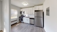 Located at 555 Main St in Chatham, NJ, this well-appointed 1-bedroom, 1-bathroom unit offers a clean, modern aesthetic across a thoughtfully designed single-floor layout. Throughout the living spaces, durable wood-look flooring in a warm gray tone provides a cohesive and contemporary foundation. The living area is bright and open, featuring neutral light gray walls, white trim, and multiple windows fitted with slatted blinds that invite generous natural light. A baseboard radiator beneath one of the windows ensures efficient heating, while a structural column subtly defines the transition between spaces.

The kitchen is a standout feature, outfitted with crisp white shaker-style cabinetry extending to the ceiling for ample storage. A full suite of stainless steel appliances — including a gas range, built-in microwave, dishwasher, and refrigerator — completes the functional and stylish cooking space, accented by a window above the sink for added natural light.

The bedroom is generously proportioned, with the same neutral palette and wood-look flooring, offering a calm and restful atmosphere. The bathroom features a full tub-shower combination enclosed by a curved rod, elegantly tiled in large-format marble-look subway tile with chrome fixtures, and a window for natural ventilation.