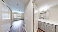 Located at 219 E Garfield St in Seattle's vibrant Capitol Hill neighborhood, this efficient single-floor unit offers a well-organized layout comprising a living room, a full bathroom, and a utility room. The living area is the heart of the space, showcasing warm-toned hardwood flooring that extends throughout and crisp white walls that keep the interior feeling bright and clean. Recessed lighting supplements the natural light that filters in through a side window fitted with blinds, while a full-width sliding glass door opens directly to an outdoor patio area, bringing in abundant greenery views and fresh air. The open, rectangular layout of the living room provides a flexible and functional space. The bathroom is neatly appointed with a full soaking tub and shower combination, accented by marble-style wall surrounds and chrome fixtures, conveying a clean, classic aesthetic. A utility room provides practical storage and functional support space. The unit also includes a refrigerator, a mounted electrical panel, and additional utility connections visible along the wall. Clean lines, neutral tones, and durable finishes make this a straightforward, move-in-ready space well-suited to urban living in Seattle.