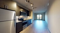 This well-appointed single-floor unit showcases a thoughtfully designed open-concept layout, seamlessly connecting the kitchen and living area. The kitchen is a standout feature, outfitted with dark navy and espresso-toned cabinetry, granite countertops, a herringbone-patterned tile backsplash, and a full suite of stainless steel appliances including a refrigerator, electric range, microwave, and dishwasher. Artistic track lighting overhead adds both style and function to the culinary space.

The living area extends naturally from the kitchen, featuring light wood-style flooring throughout and neutral-toned walls that create a bright, airy atmosphere. French doors open to a private balcony, inviting natural light and outdoor views into the space.

The bedroom is a comfortable retreat, carpeted for warmth and equipped with a ceiling fan and window blinds that allow for natural light and privacy. The full bathroom is finished in a clean, contemporary style with white quartz countertops, dark cabinetry, large-format white tile flooring, and a full tub-shower combination. A dedicated in-unit laundry area with a stacked washer and dryer adds a practical convenience to this well-rounded space.