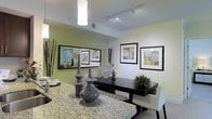 This single-floor residence showcases a thoughtfully designed interior that blends modern aesthetics with functional living. The dining area serves as a central highlight, featuring a sleek dark dining table set atop a patterned area rug and complemented by a stunning granite-topped surface that adds a touch of luxury. Decorative ceramic vases and curated tabletop accessories lend an artistic flair to the space.

The walls are adorned with a curated gallery of framed artwork, contributing to a polished and sophisticated ambiance. A large mirror further enhances the sense of openness, reflecting light and visual depth throughout the room. Track lighting runs along the ceiling, providing flexible and effective illumination, while a contemporary pendant light fixture adds a warm, focused glow to the dining area.

The ceilings feature clean lines accented by visible ductwork detailing, lending an urban, modern character to the interior. Neutral wall tones in soft green-white hues create a calm and inviting backdrop that allows the furnishings and décor to stand out. Overall, this residence offers a well-appointed, move-in-ready living environment with a cohesive design sensibility that is both elegant and practical.