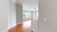 This thoughtfully designed 2-bedroom, 1-bathroom residence offers a comfortable and functional single-floor layout. The open-concept kitchen and living area serves as the heart of the home, featuring warm hardwood flooring, crown molding, and a ceiling fan. Large windows and a sliding glass door flood the space with natural light and provide access to a private balcony with exterior views. The kitchen is well-equipped with white cabinetry, granite countertops, a decorative tile backsplash, stainless steel appliances including a range, over-the-range microwave, and a large side-by-side refrigerator, all set over light-toned tile flooring. An in-unit washer is conveniently positioned at the transition between the kitchen and living areas. Both bedrooms feature plush carpeting, crown molding, and textured ceilings, with the primary bedroom offering a walk-in closet with built-in shelving and an adjacent bathroom featuring tile flooring and vanity storage. The second bedroom also benefits from natural light through a window with blinds. A hallway connects all rooms, contributing to a cohesive and efficient flow throughout the residence.