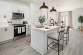 This single-story residence in Huntsville, Alabama, presents a cohesive modern design characterized by a bright, neutral color palette, light wood-look flooring, and clean architectural lines. The open-concept kitchen serves as a central hub of the space, anchored by a large island with a white quartz countertop, an undermount sink with a matte black faucet, and bar seating for casual dining. Overhead, two bold black dome pendant lights add a striking contrast to the crisp white cabinetry. The kitchen is equipped with stainless steel appliances, a marble-style tile backsplash, and ample cabinet storage with matte black hardware. The layout flows naturally into the living area, which features a pair of glass-paneled doors that invite abundant natural light and outdoor views. The bedrooms are well-proportioned and restful, each featuring ceiling fans, neutral walls, and windows that bring in natural light. The primary bathroom includes a glass-enclosed walk-in shower with marble-style tile surround and direct access to a walk-in closet with built-in shelving. A dedicated entryway nook with a built-in bench provides a practical and welcoming arrival area. Throughout, the consistent use of light tones and modern fixtures creates a polished, cohesive ambiance.
