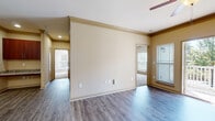 This single-story residence offers a thoughtfully designed layout connecting living, dining, and kitchen areas in an open, cohesive flow. The entryway features a decorative arched alcove and column detail, setting an inviting tone upon arrival. The living area is finished with wood-style plank flooring, crown molding, and a ceiling fan, while a sliding glass door opens to a private balcony with views of surrounding greenery, allowing natural light to fill the space.

The kitchen is equipped with rich, dark wood cabinetry, granite-style countertops, a tile backsplash, and a full suite of stainless steel appliances including a refrigerator, range, and over-the-range microwave. A peninsula counter connects the kitchen to the main living area, making it well-suited for both cooking and entertaining.

The bedrooms feature plush carpeting, ceiling fans, and ample natural light from windows with blinds. The primary bedroom includes a spacious walk-in closet with built-in shelving. The bathroom is appointed with matching dark wood cabinetry, granite-style countertops, wood-style flooring, a soaking tub, and a tiled shower with decorative accent tiles.
