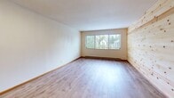 Located in Seattle's Greenwood neighborhood, this one-bedroom, one-bathroom unit offers a well-organized, single-floor layout with consistent light wood laminate flooring throughout. The combined kitchen and living area forms the heart of the space, highlighted by a striking natural pine shiplap accent wall that adds warmth and texture. Large windows invite abundant natural light and provide pleasant views of the surrounding neighborhood's greenery. The kitchen is equipped with warm-toned wood cabinetry, white countertops, and a full-size refrigerator, offering functional storage and preparation space. A hallway connects the main living area to the private quarters, lined with sleek, dark wood-paneled sliding closet doors — one of three closets found throughout the unit, providing ample storage. The bedroom is a comfortable, well-proportioned room with a window and its own sliding-door closet. The bathroom features light wood-toned cabinetry with a white countertop vanity, a tub-shower combination with white tile surround, chrome fixtures including grab bars, and light wood flooring that ties the space together. Baseboard heating is present throughout the unit, ensuring comfort year-round.