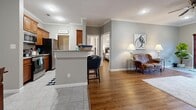 Located at 10801 Paul Eells Drive in North Little Rock, Arkansas, this thoughtfully designed one-bedroom, one-bathroom residence offers a comfortable and functional single-floor layout. The open living area features warm hardwood-style flooring and crown molding, creating an inviting atmosphere. A kitchen peninsula with bar seating connects the galley-style kitchen to the main living space, where rich wood cabinetry, granite-look countertops, and stainless steel appliances provide a practical yet stylish cooking environment. Tile flooring runs throughout the kitchen for easy maintenance. The adjacent dining area, finished with tile flooring and crown molding, provides a defined space for meals. The living room offers a relaxed setting with a fireplace and wall-mounted television as focal points. The generously sized bedroom features hardwood-style flooring, a ceiling fan, and access to a dedicated closet with built-in hanging storage. The full bathroom is finished with granite-look tile surround and a tub-shower combination, complemented by a wood-toned vanity. A dedicated laundry room with overhead cabinetry accommodates a full-size washer and dryer, adding everyday convenience to this well-rounded residence.