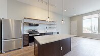 Located in the heart of downtown Columbus at 150 N 3rd St, this contemporary single-floor residence offers a well-designed open-concept layout with high-end finishes throughout. The kitchen is a standout feature, showcasing dark espresso cabinetry, stainless steel appliances, a classic white subway tile backsplash with open wood shelving, a matte black faucet, and a large center island topped with light quartz countertops. Globe pendant lights hang above the island, complementing the track lighting that runs along the elevated ceiling, where exposed ductwork adds an industrial touch. Warm-toned hardwood-style flooring flows seamlessly throughout the space, enhancing the cohesive aesthetic. The living area benefits from generous natural light streaming through expansive floor-to-ceiling windows that frame striking views of the Columbus skyline and surrounding downtown architecture. The bedroom is spacious and bright, with large windows that continue to deliver panoramic city views. The bathroom is clean and modern, featuring a walk-in shower with white paneled surround and oil-rubbed bronze fixtures. A dedicated in-unit laundry area with side-by-side washer and dryer adds everyday convenience. This space combines urban sophistication with functional living in a prime downtown Columbus location.