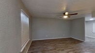 This two-story home is thoughtfully designed with consistent finishes and functional layouts across both floors. The main level features a welcoming living area with wood-look laminate flooring, neutral gray walls, a ceiling fan with integrated lighting, and a window fitted with horizontal blinds that allows natural light to filter in. A staircase with white railings connects the two levels, and the entryway opens to a corridor leading to additional rooms. The kitchen is a standout space, featuring white shaker-style cabinetry with matte black hardware, light granite countertops, a single-basin sink with a black faucet, and stainless steel appliances including a range and refrigerator. The lower level also includes a half bathroom tucked beneath the staircase, characterized by a sloped ceiling and oil-rubbed bronze fixtures. Upstairs, the bedrooms are generously sized with the same wood-look flooring, ceiling fans, and windows providing natural light. The full bathroom on the upper level is finished in white, featuring a vanity with white cabinetry, a framed mirror with industrial-style lighting, and a tub-shower combination. Throughout, textured ceilings and clean white baseboards contribute to a cohesive, move-in-ready aesthetic.