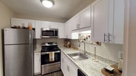 This single-story residence offers a thoughtfully designed layout with cohesive finishes across all rooms. The kitchen is a functional centerpiece, outfitted with white shaker-style cabinetry, granite-look countertops, stainless steel appliances including a refrigerator, electric range, and over-the-range microwave, and a stainless steel sink with a modern faucet. Dark wood-style flooring runs through the kitchen, living, and dining areas, adding warmth and continuity.

The living room is bright and welcoming, anchored by a large window that draws in natural light, with ample space for multiple seating arrangements. An adjacent dining area accommodates a full dining set beneath a pendant light fixture. The primary bedroom features plush carpeting, a generous window, and a textured ceiling, creating a comfortable retreat. A second bedroom offers carpeted flooring, a window with vertical blinds, and versatile space. The bathrooms are finished with granite-look countertops, large mirrors, and shower-tub combinations, maintaining a consistent and polished aesthetic throughout the home.