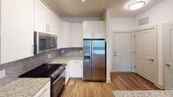 Located at 8940 Rachel Freeman Way in Charlotte, NC, this single-floor unit offers a clean, contemporary design with consistent wood-style flooring running throughout the entire space. The kitchen serves as a functional centerpiece, featuring white shaker-style cabinetry with brushed nickel hardware, granite countertops, and a mosaic tile backsplash. A full suite of stainless steel appliances includes a side-by-side refrigerator with ice and water dispenser, electric range, over-the-range microwave, and dishwasher. The open layout connects the kitchen to the living and dining areas, with the hallway leading to additional rooms and a front entry door. The bedroom areas are bright and neutral, each equipped with ceiling fans and windows fitted with blinds that allow natural light while maintaining privacy. The bathroom features a glass-enclosed shower, wood-style flooring, granite-topped vanity, and direct access to a walk-in closet with built-in shelving and hanging rods. Throughout the unit, crisp white walls, clean baseboards, and a neutral color palette create a cohesive and move-in-ready atmosphere well-suited to a variety of lifestyles.
