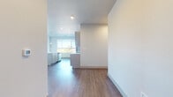 This single-floor space showcases a clean, contemporary design with a neutral color palette, hardwood-style flooring, and an abundance of natural light throughout. The open-concept living area is generously sized, featuring multiple large windows and a sliding door to a balcony, framing expansive outdoor views of surrounding trees and distant landscapes. A ceiling fan adds both function and a finishing touch to this bright, airy space.

The kitchen is well-appointed with grey cabinetry, stainless steel appliances including a refrigerator, electric range, and microwave, complemented by a white subway tile backsplash and light countertops. A central island with an integrated sink and pendant lighting above provides additional workspace and a natural gathering point.

The bedrooms are carpeted for comfort, each featuring large windows with scenic views and ceiling fans. Sliding panel closet doors offer practical storage solutions. The bathroom includes a dual-sink vanity with white countertops, grey cabinetry, hardwood-style flooring, and a well-placed mirror, creating a clean and functional environment. Throughout, the space maintains a cohesive, modern aesthetic with consistent finishes and thoughtful design details.