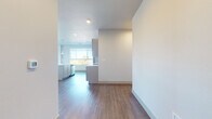 This single-floor space showcases a clean, contemporary design with a neutral color palette, hardwood-style flooring, and an abundance of natural light throughout. The open-concept living area is generously sized, featuring multiple large windows and a sliding door to a balcony, framing expansive outdoor views of surrounding trees and distant landscapes. A ceiling fan adds both function and a finishing touch to this bright, airy space.

The kitchen is well-appointed with grey cabinetry, stainless steel appliances including a refrigerator, electric range, and microwave, complemented by a white subway tile backsplash and light countertops. A central island with an integrated sink and pendant lighting above provides additional workspace and a natural gathering point.

The bedrooms are carpeted for comfort, each featuring large windows with scenic views and ceiling fans. Sliding panel closet doors offer practical storage solutions. The bathroom includes a dual-sink vanity with white countertops, grey cabinetry, hardwood-style flooring, and a well-placed mirror, creating a clean and functional environment. Throughout, the space maintains a cohesive, modern aesthetic with consistent finishes and thoughtful design details.