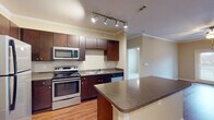 This single-floor residence offers a thoughtfully designed layout that balances comfort and functionality throughout. The open-concept living and dining area is finished with warm hardwood flooring and crown molding, creating a polished, cohesive aesthetic. Track lighting overhead adds a modern touch and ensures the space is well-illuminated.

The kitchen is a standout feature, equipped with rich dark-wood cabinetry extending to the ceiling for ample storage, granite-style countertops, and a full suite of stainless steel appliances including a refrigerator, electric range, microwave, and dishwasher. A peninsula with additional counter space provides a convenient area for meal preparation or casual dining.

The bedroom areas are carpeted for comfort and receive natural light through blinded windows. The primary bathroom is generously proportioned, featuring a dark-wood vanity with granite-style countertops, a large mirror, tile flooring, and direct access to a spacious walk-in closet with built-in shelving. A secondary bathroom includes a full soaking tub and shower combination with neutral tile flooring.

Throughout the residence, consistent design elements — including crown molding, neutral warm-toned walls, and coordinated fixtures — contribute to a clean, unified atmosphere.