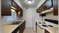Located at 33 Meeting House Rd in Centerville, Ohio, this single-floor residence offers a functional and straightforward layout well-suited for comfortable everyday living. The galley-style kitchen is efficiently designed with dark wood cabinetry lining both walls, providing ample upper and lower storage. It includes a double-basin stainless steel sink, a dishwasher, a coil-top electric range, and a full-size refrigerator, all set atop light-toned tile flooring. The living area features wall-to-wall carpeting and a sliding glass door with vertical blinds that opens to an outdoor view, allowing natural light to fill the room. Beam detailing along the ceiling adds a subtle architectural element to the space. The bedrooms are carpeted and offer a quiet, neutral atmosphere; one includes a ceiling fan with light fixture and a window with blinds that brings in additional natural light. Closet access is provided in the bedroom areas. The bathroom features a vanity with under-cabinet storage, a large wall mirror, and tile backsplash detailing, maintaining a clean and practical aesthetic throughout. The overall layout, as seen from the dollhouse view, presents a well-organized floor plan with clear separation between the kitchen, living, sleeping, and bathroom areas.