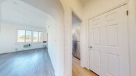 Located at 437 N Ardmore Ave in Los Angeles, this well-appointed unit offers a thoughtfully designed single-floor layout comprising a living room, kitchen, bathroom, hallway, and closet. The living room is bright and open, featuring light wood-tone flooring, crisp white walls, and multiple windows fitted with horizontal blinds that invite generous natural light and offer views of the surrounding neighborhood's treetops and skyline. An elegant arched doorway connects the living area to the hallway, adding a charming architectural detail to the space. The galley-style kitchen is efficiently arranged with white shaker cabinetry, dark countertops, a stainless steel double-basin sink, a gas range, and a full-size stainless steel refrigerator. A decorative sputnik-style chandelier and a iridescent mosaic tile backsplash lend a stylish touch, while a window at the end of the kitchen provides additional natural light. The bathroom is clean and classically finished with white subway tile surrounding a full bathtub with shower, penny-round tile flooring, and a small window for ventilation. Throughout the unit, the consistent light wood flooring and white walls create a cohesive, airy aesthetic that maximizes the sense of space.