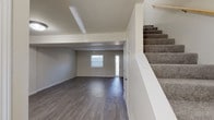This well-maintained two-floor home offers a thoughtfully designed layout with a blend of practical finishes and modern touches throughout. The main level features a welcoming entryway with a front door flanked by a window that brings in natural light, opening into a spacious living area with dark hardwood-style flooring and neutral gray walls. A carpeted staircase leads to the upper level, while a half bathroom with a dark-cabinetry vanity and white countertop is conveniently located near the kitchen. The kitchen is a standout feature, offering white cabinetry, stone-look countertops, light wood-style flooring, and a full suite of stainless steel appliances including a refrigerator, range, microwave, and dishwasher. An open pass-through connects the kitchen to a bright dining or flex space. The upper level hosts generously sized bedrooms finished with plush gray carpet and crisp white trim, providing a comfortable and quiet retreat. A full bathroom on the upper level includes a tub-shower combo, white fixtures, and a dark-cabinetry vanity consistent with the home's cohesive design. Throughout the home, neutral tones and clean lines create a bright, move-in-ready atmosphere.