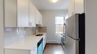 Located in Boston, MA, this single-floor residence offers a thoughtfully updated interior with a clean, modern aesthetic throughout. The galley-style kitchen is a standout feature, showcasing white shaker cabinetry, light quartz countertops, a grey subway tile backsplash, and stainless steel appliances including a refrigerator, dishwasher, and range. A window above the counter draws in natural light and provides an exterior view, enhancing the kitchen's bright and functional feel. Dark hardwood flooring in the kitchen transitions to warm-toned hardwood floors throughout the living and bedroom areas, lending a cohesive and inviting character to the space. The bathroom is elegantly finished with large-format marble-look tile in the walk-in shower, fitted with sliding glass doors, complemented by slate-toned floor tiles and crisp white fixtures. The bedroom is generously proportioned with soft neutral walls, ample natural light, and convenient in-unit laundry housed in a dedicated closet alongside an additional storage closet. The overall design balances contemporary finishes with practical functionality, making this Boston residence a well-equipped and comfortable living space.