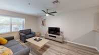 Located at 8067 Dream Catcher Circle in Naples, Florida, this two-story home offers a practical and comfortable layout across two floors. The main level features light tile flooring throughout, a bright entry hallway adorned with decorative artwork, and a seamless flow between the combined living, dining, and kitchen areas. The kitchen is well-equipped with warm wood cabinetry, stone-look countertops, stainless steel appliances including a French door refrigerator, and recessed lighting overhead. A separate dining area accommodates a full dining table beneath an elegant chandelier, adjacent to the staircase leading to the upper level. The living room features wood-look flooring and a clean, neutral palette. A dedicated laundry room on the main level houses a full-size washer and dryer with overhead shelving. Three bathrooms serve the home, including one with a glass-enclosed walk-in shower and a windowed powder room. Upstairs, the spacious primary bedroom includes a ceiling fan, plush carpet, and a walk-in closet, while the second bedroom mirrors the same cozy, well-lit character with a ceiling fan and natural light from a large window. Neutral tones and consistent finishes throughout create a cohesive, move-in-ready atmosphere.