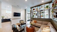 Located in Charlotte, NC, this thoughtfully designed single-floor space combines a living room and dining area into a cohesive, modern communal environment. The layout flows seamlessly from one zone to the next, unified by warm herringbone-patterned hardwood flooring throughout.

The living area is anchored by a large sectional sofa paired with leather accent chairs and wooden coffee tables, creating an inviting gathering space. Floor-to-ceiling open shelving, mounted on industrial-style black iron frames against sage green shiplap walls, displays an artful mix of plants, books, and curated décor. Recessed lighting and large windows flood the space with natural light, offering views to the outdoors.

The dining zone features built-in booth seating with upholstered gray banquettes framed by sage green shiplap columns, accompanied by dark pedestal tables and pendant lighting overhead. A bold patterned accent wall and round mirror add visual interest. A separate dining nook showcases a live-edge wood table surrounded by upholstered chairs, with a gallery of framed artwork adorning the crisp white walls.

A welcoming entry area with long built-in bench seating, open shelving lined with greenery, and a set of black-framed glass doors connects the interior to the outside, enhancing the bright, airy ambiance throughout.