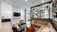 Located in Charlotte, NC, this thoughtfully designed single-floor space combines a living room and dining area into a cohesive, modern communal environment. The layout flows seamlessly from one zone to the next, unified by warm herringbone-patterned hardwood flooring throughout.

The living area is anchored by a large sectional sofa paired with leather accent chairs and wooden coffee tables, creating an inviting gathering space. Floor-to-ceiling open shelving, mounted on industrial-style black iron frames against sage green shiplap walls, displays an artful mix of plants, books, and curated décor. Recessed lighting and large windows flood the space with natural light, offering views to the outdoors.

The dining zone features built-in booth seating with upholstered gray banquettes framed by sage green shiplap columns, accompanied by dark pedestal tables and pendant lighting overhead. A bold patterned accent wall and round mirror add visual interest. A separate dining nook showcases a live-edge wood table surrounded by upholstered chairs, with a gallery of framed artwork adorning the crisp white walls.

A welcoming entry area with long built-in bench seating, open shelving lined with greenery, and a set of black-framed glass doors connects the interior to the outside, enhancing the bright, airy ambiance throughout.