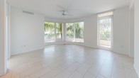 This well-appointed single-floor residence offers a clean, modern aesthetic throughout, characterized by crisp white walls, light-toned tile flooring in the main living areas, and an abundance of natural light. The open-concept kitchen is a standout feature, showcasing rich walnut-toned cabinetry, dark granite countertops, and a full suite of stainless steel appliances including a French door refrigerator, electric range, and built-in microwave. A raised peninsula counter separates the kitchen from the living area, creating a natural flow between spaces. The spacious living area is highlighted by a dramatic curved bay window framing lush tropical greenery, complemented by a ceiling fan and direct access to an outdoor balcony. The bedrooms feature warm wood-look flooring and generous windows with blinds, providing ample natural light and a comfortable ambiance. The primary bathroom offers a glass-enclosed walk-in shower and a wood-paneled vanity with a dark granite countertop, while the secondary bathroom includes a full soaking tub with tiled surround and a matching vanity. A dedicated laundry area houses a full-sized washer and dryer. The 3D floorplan reveals a thoughtfully designed layout with arched architectural detailing near the entry.