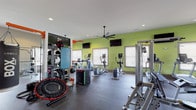 Located at 6701 Fox Rd in Raleigh, NC, this fitness center offers a comprehensive, single-floor workout facility designed to accommodate a wide range of exercise needs. The space is defined by its energetic lime-green accent walls, neutral gray tones, and durable rubberized flooring throughout, creating a functional yet visually stimulating environment. Multiple large ceiling fans are suspended overhead, ensuring steady airflow across the open workout floor.

The cardio zone is well-appointed with treadmills, elliptical trainers, a rowing machine, and stationary bikes, all positioned near windows fitted with horizontal blinds that allow natural light to filter in. Wall-mounted flat-screen televisions are positioned throughout this area for entertainment during workouts.

The strength training section features a robust selection of cable machines, multi-station cable systems, and weight benches, supplemented by a full rack of dumbbells displayed in front of a large wall mirror. A dedicated free weights and functional training area includes a mini trampoline, medicine balls, and a wall-mounted storage rack stocked with accessories.

An entry area provides built-in cubby shelving for personal belongings, a water fountain, and access to restroom facilities. Recessed lighting and large windows contribute to a bright, well-ventilated atmosphere throughout the space.