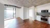 Located along the iconic Sunset Strip at 8500 W Sunset Blvd in West Hollywood, this single-floor residence blends industrial design with modern sophistication. The open living area makes a striking impression with its exposed concrete ceiling, warm hardwood flooring throughout, and expansive floor-to-ceiling windows that flood the space with natural light and frame sweeping views of the surrounding cityscape.

The kitchen is outfitted with high-gloss white cabinetry extending to the ceiling, sleek quartz countertops, a gray tile backsplash, a stainless steel double sink, and Bosch stainless steel appliances including an electric range and over-the-range microwave. Subtle ambient lighting traces the upper cabinetline, adding a refined finishing touch.

The bedroom offers generous proportions, complete with a large closet for ample storage, and direct access to the bathroom. A second closet space is also present in the unit. The bathrooms are finished in crisp white large-format tile, featuring soaking tubs with overhead rain showers, glass enclosures, recessed niche shelving, and warm wood-toned vanities with clean-lined chrome fixtures.

Throughout the unit, the interplay of raw concrete, natural wood, and clean white walls creates a cohesive, contemporary aesthetic well-suited to the energy of West Hollywood.