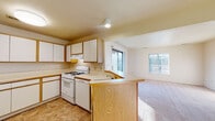 Located at 2210 E Cork St in Kalamazoo, Michigan, this single-floor home offers a practical and comfortable layout designed for everyday living. The open-concept design connects the kitchen and living area seamlessly, creating a spacious, airy feel throughout. The kitchen is well-appointed with abundant white cabinetry trimmed in warm oak, generous counter space, a gas range, and a built-in sink. A peninsula with oak paneling serves as a natural divider between the kitchen and the adjoining living space, offering additional workspace and easy flow between areas. Tile flooring in the kitchen provides durability, while the living area transitions to soft, neutral-toned carpeting that extends into the rest of the home. Natural light streams in through multiple windows, brightening the interior throughout the day. The living space is notably open and versatile, with clean walls and a simple, functional layout. Bedroom areas feature wide bifold closet doors, providing ample storage. The bathroom includes a wood-toned vanity with a large mirror, white countertop, and a tub-shower combination. Overall, the home presents a clean, move-in ready environment with a neutral palette well-suited for a variety of living arrangements.
