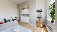 Located at 1228 Spruce Street in Philadelphia's Center City neighborhood, this efficiently designed one-bedroom, one-bathroom unit makes excellent use of its compact footprint. The open-concept main room serves as both a living and sleeping area, anchored by two large arched windows that flood the space with natural light and offer sweeping views of the Philadelphia skyline. Light hardwood flooring runs throughout, contributing to a clean, airy aesthetic.

The kitchenette is neatly integrated into the main room, featuring white shaker-style cabinetry, a countertop gas range, a stainless steel refrigerator, a microwave, and a single basin sink — providing all essential cooking amenities in a streamlined footprint. A small dining area with a round table and chair is tucked near the entry hallway, making efficient use of available space.

The bathroom is finished in a bright, all-white palette and includes a bathtub with overhead shelving. An adjacent closet provides dedicated storage. The entry hallway connects all areas of the unit smoothly, enhancing the overall flow.

The crisp white walls, minimalist design, and abundant natural light create a clean, modern ambiance throughout, making this unit a highly functional and well-appointed space in the heart of Philadelphia.