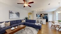Located at 8585 Sienna Springs Blvd in Missouri City, TX, this single-story residence offers a well-designed open-concept layout that seamlessly connects the main living spaces. The living room features vaulted ceilings with a ceiling fan, warm hardwood-style flooring, and ample natural light, creating an inviting and airy atmosphere throughout.

The kitchen is appointed with rich dark cabinetry, light granite countertops, black appliances including a range, built-in microwave, and refrigerator, and a curved breakfast bar with pendant lighting overhead. Track lighting adds a modern touch to this functional and stylish culinary space. Adjacent to the kitchen, a sun-filled dining nook benefits from a generous bay window arrangement, flooding the area with natural light.

The bedrooms are comfortably sized, featuring plush carpeting, ceiling fans, and windows that allow for plenty of natural light. The bathroom connects directly to the bedroom and includes a dark-cabinet vanity with a white countertop and dual sinks. A dedicated in-unit laundry room houses a full-size washer and dryer with overhead shelving for added convenience. Throughout the home, the consistent use of hardwood-style flooring, neutral tones, and arched architectural details contribute to a cohesive and polished aesthetic.
