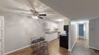 This single-floor unit offers a functional and well-organized layout across several distinct spaces. The living area is spacious and finished with durable wood-look flooring, neutral gray walls, and a textured ceiling. A ceiling fan with integrated lighting serves the adjoining dining area, which comfortably accommodates a small dining set. A sliding glass door leads to a private balcony, allowing natural light to fill the space and providing outdoor views of surrounding greenery.

The kitchen follows a galley-style configuration, featuring white raised-panel cabinetry on both sides, gray laminate countertops, a stainless steel sink, and black appliances including a refrigerator and range. The layout maximizes storage and counter space efficiently.

Two bedrooms are finished with wall-to-wall carpet and neutral paint, each receiving natural light through windows with views of the outdoors. One bedroom includes a closet and connects conveniently to the hallway. The full bathroom includes a single-sink vanity with gray countertops, white cabinetry, a large mirror, and a shower-tub combination. Wood-look flooring carries through the bathroom, complementing the clean, cohesive aesthetic found throughout the unit.