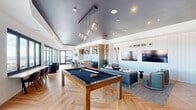 Located at 66 S Van Gordon St in Lakewood, Colorado, this thoughtfully designed amenity lounge offers a well-rounded social and work environment across a single, open floor. The space is anchored by a striking game area centered around a full-size pool table beneath a sleek geometric pendant light fixture, complemented by a dark, high-gloss ceiling that creates a sophisticated contrast with the warm herringbone hardwood flooring found throughout.

The lounge area features a shiplap accent wall adorned with ski-themed décor, dual large-screen televisions, and comfortable seating including curved upholstered chairs with bold accent stripes — evoking a mountain resort ambiance. A rustic stone column adds a natural, textural element to the space.

The kitchenette is equipped with a stainless steel sink, microwave, open shelving with curated décor, and a textured herringbone tile backsplash. Adjacent to it, a generous high-top communal work table with modern cantilever bar stools provides a functional co-working area.

Floor-to-ceiling windows flood the space with natural light and frame sweeping panoramic views of the Lakewood skyline and the Rocky Mountain foothills beyond, making it an inspiring setting for both work and relaxation.