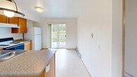 Located at 3428 W McLeod Rd in Marietta, WA, this two-bedroom, one-bathroom single-floor unit offers a practical and well-organized layout. The kitchen is equipped with warm oak cabinetry, granite-style laminate countertops, a coil electric range, and a refrigerator, with light tile flooring underfoot. An adjacent dining area features a sliding glass door that opens to a balcony overlooking lush greenery, bringing in natural light and outdoor views. The spacious primary bedroom is carpeted and features large windows with vertical blinds that frame views of surrounding trees, along with a baseboard heating unit. The second bedroom is similarly carpeted and includes a full-width sliding closet with wood-paneled doors. A shared full bathroom is appointed with warm oak vanity cabinetry, granite-style countertops, a large mirror, and a combination tub and shower. The living area is generously sized with soft carpet, neutral walls, and a closet with sliding wood doors. Baseboard heating is present throughout the unit. The overall aesthetic is clean and functional, with consistent warm wood tones and neutral finishes creating a cohesive and comfortable living environment.